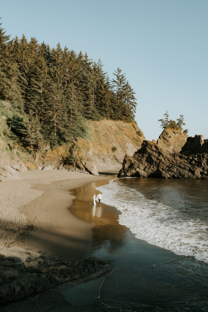 wide image of secret beach and elopement couple playing in the waves