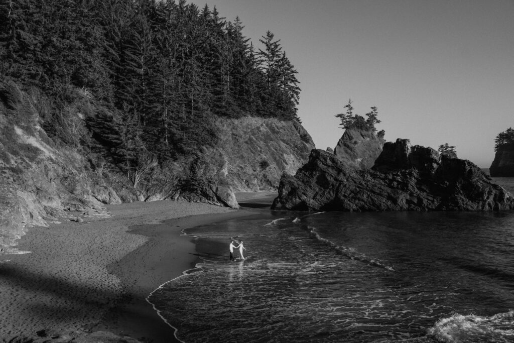 black and white of couple from afar on the oregon coast during sunset elopement