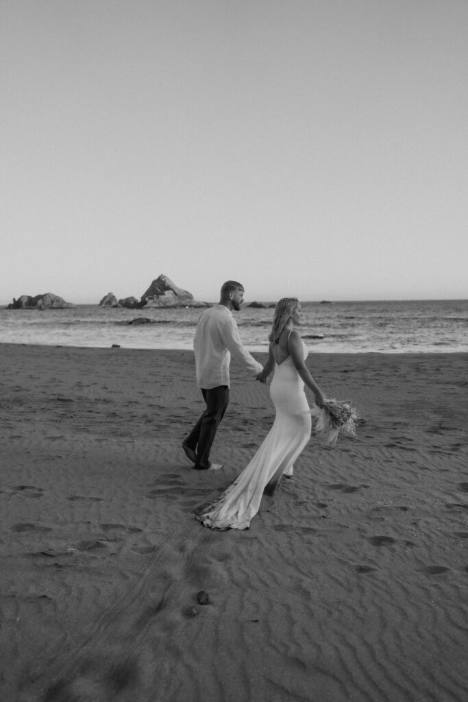 black and white of bride and groom walking on the beach