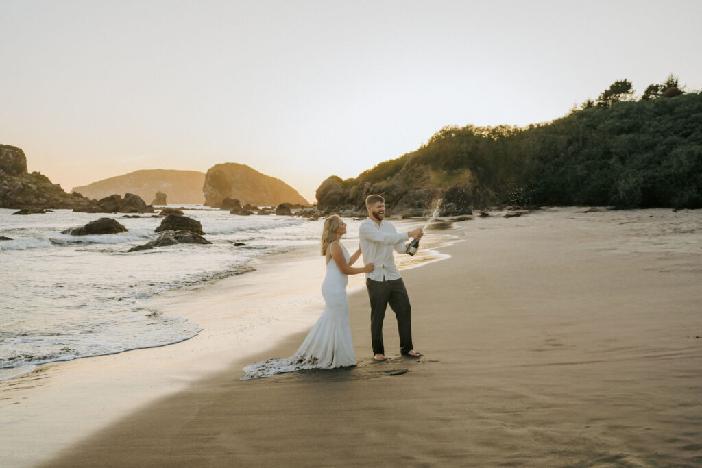 eloping couple popping champagne after elopement ceremony on the Oregon Coast at sunset