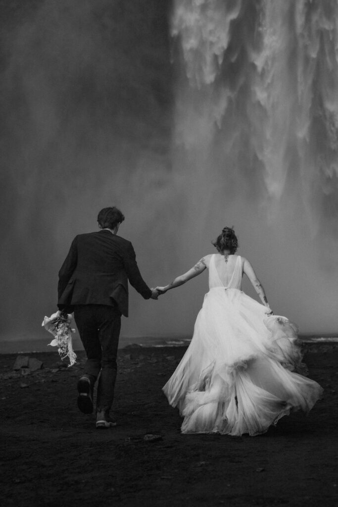 black and white of couple running toward skogafoss waterfall on elopement day in iceland