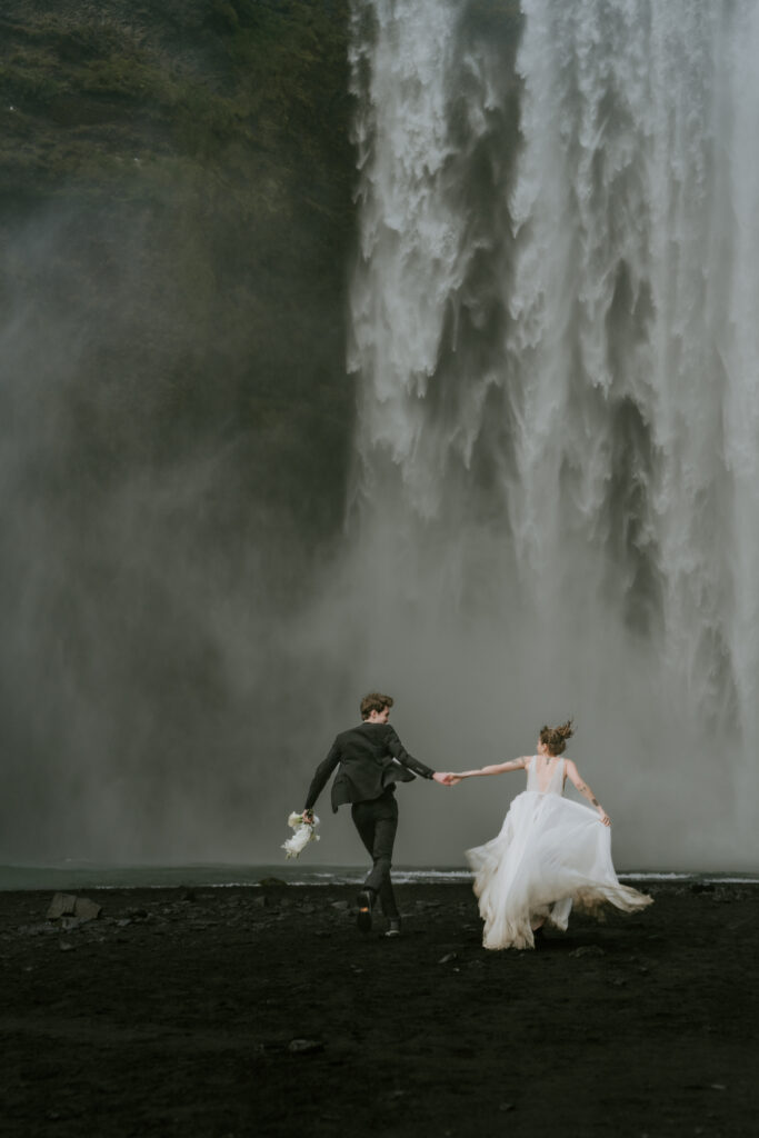 eloping couple running toward skogafoss waterfall in iceland