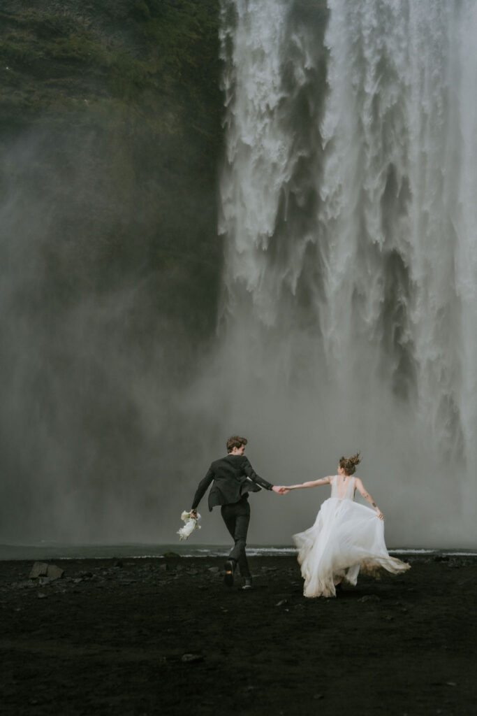 couple running enjoying the water spraying at skogafoss during iceland elopement wedding day