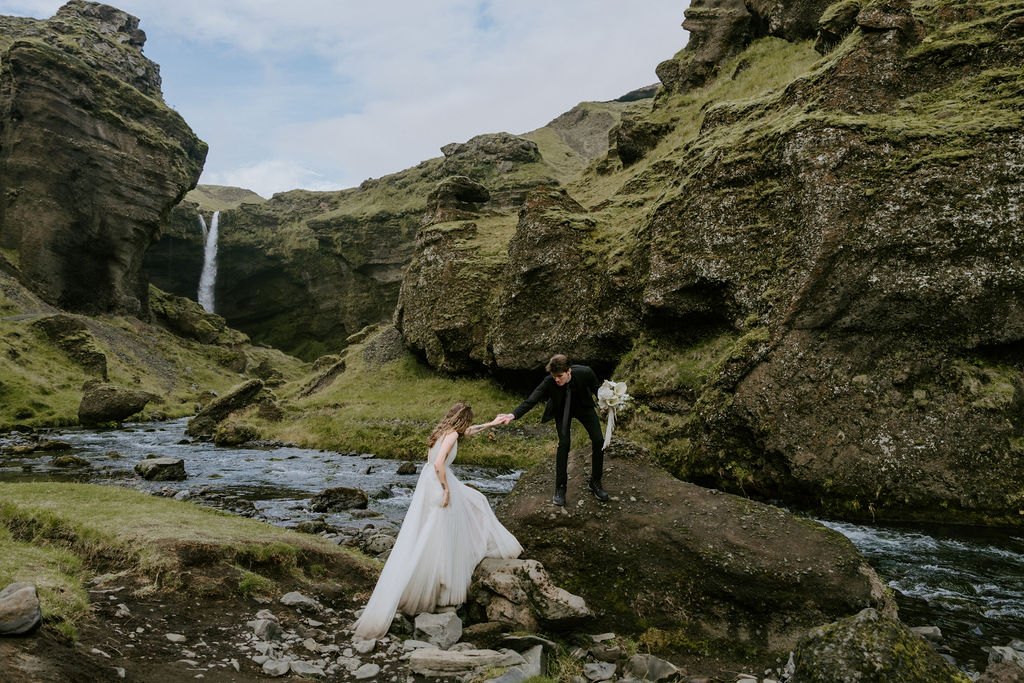 couple climbing up rock while eloping in iceland at a waterfall