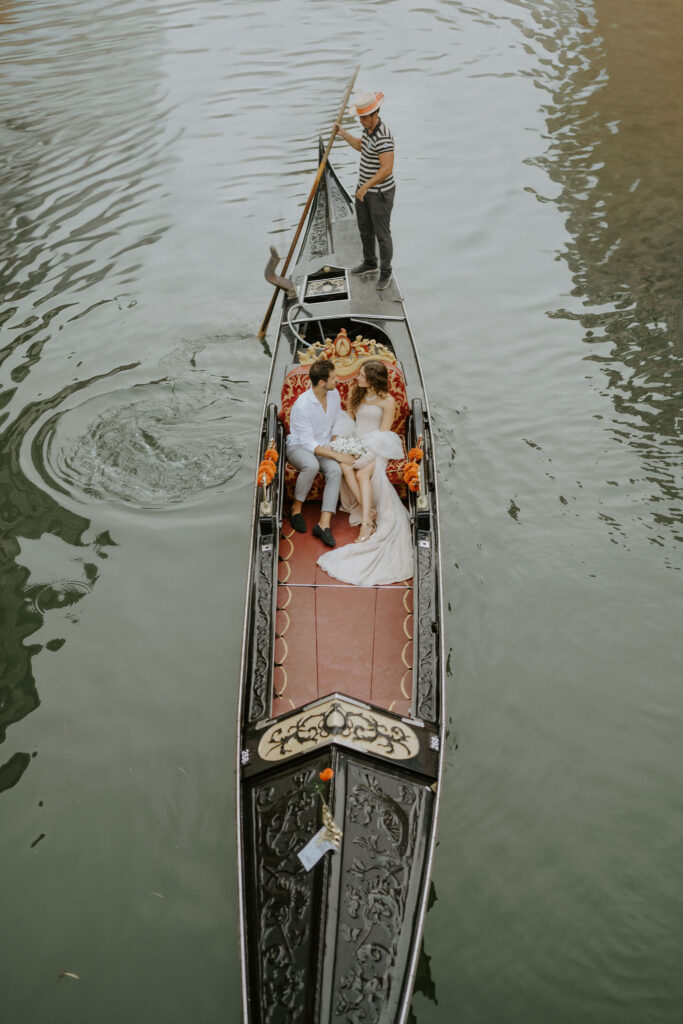 bride and groom sitting in a gondola, going down the canal during their venice elopement day
