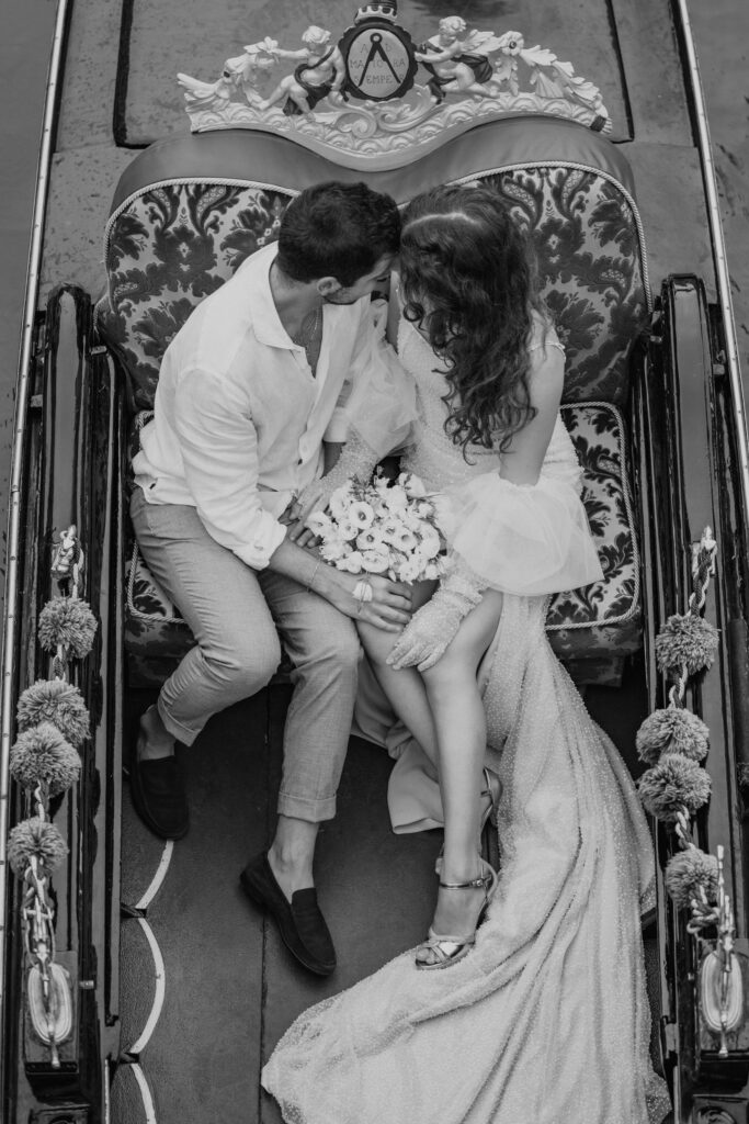 bride and groom sitting in a gondola, going down the canal during their venice elopement day