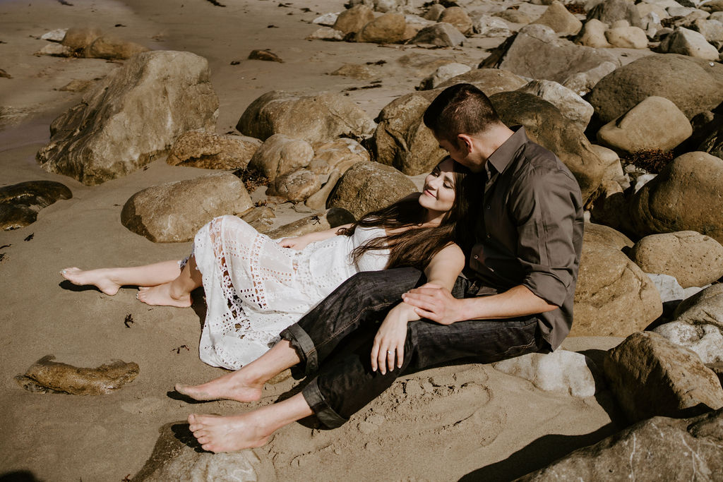 bride and groom sitting on the rocks at the beach in southern california