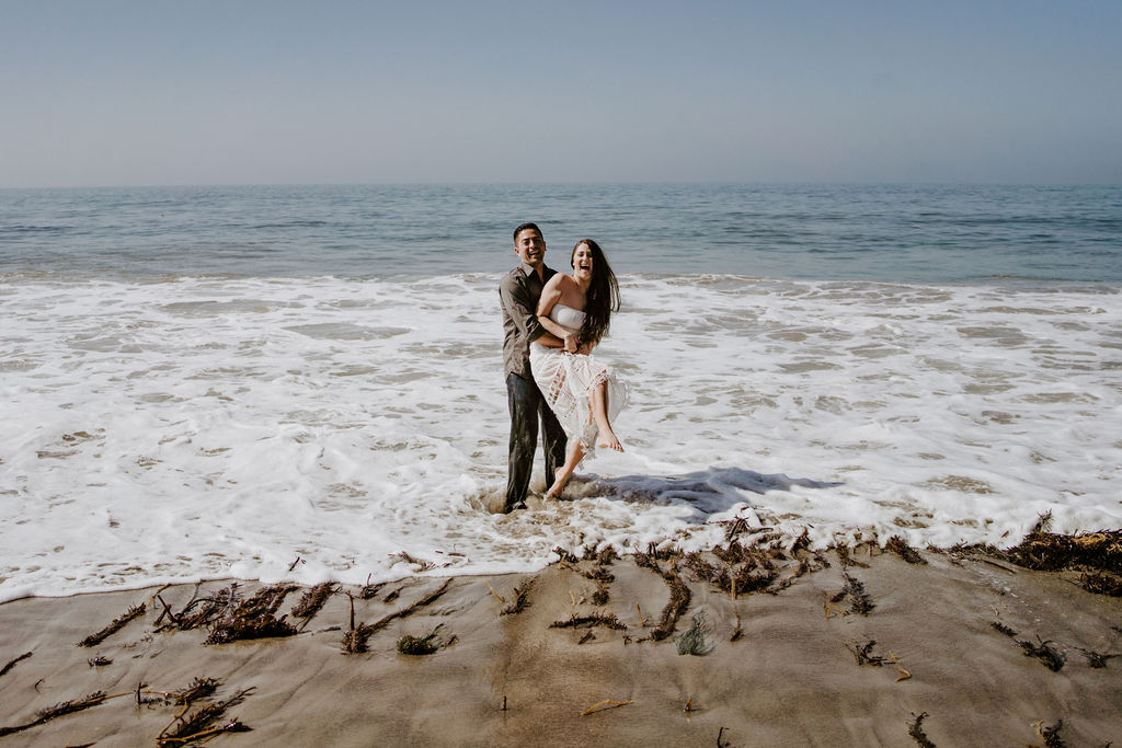 adventurous bride and groom standing in the ocean at el matador beach