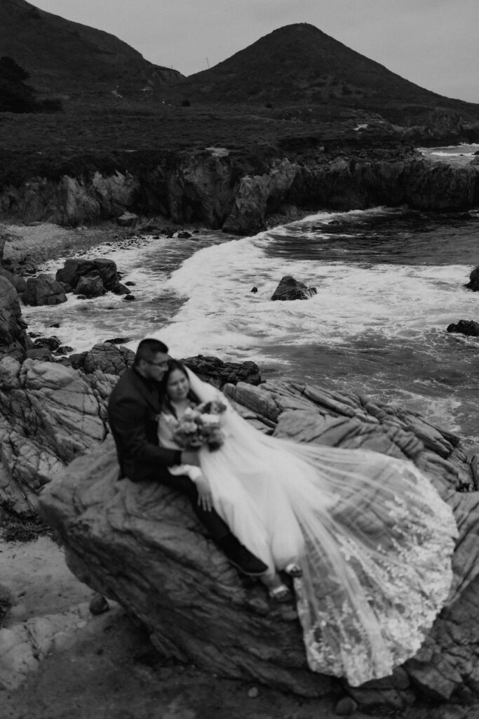 bride and groom posing on a large rock at the coast in Big Sur