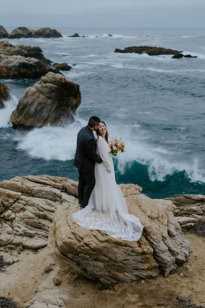 bride and groom posing on a large rock at the coast in Big Sur