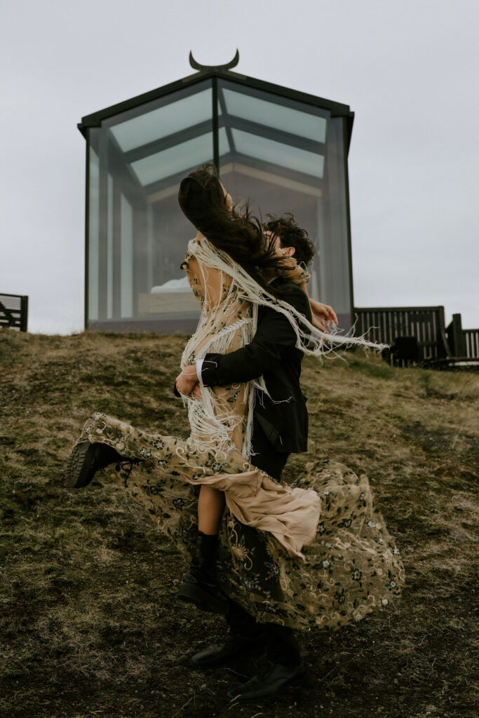 elopement couple spinning around in front of a glass cabin in Iceland Highlands