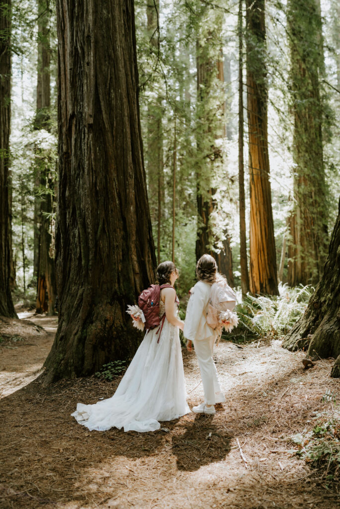 brides hiking through the forest together during their redwoods elopement