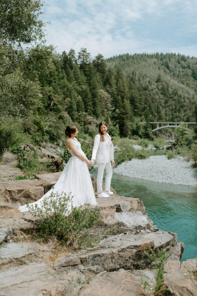 brides posing on a rocky cliff overlooking turquoise smith river