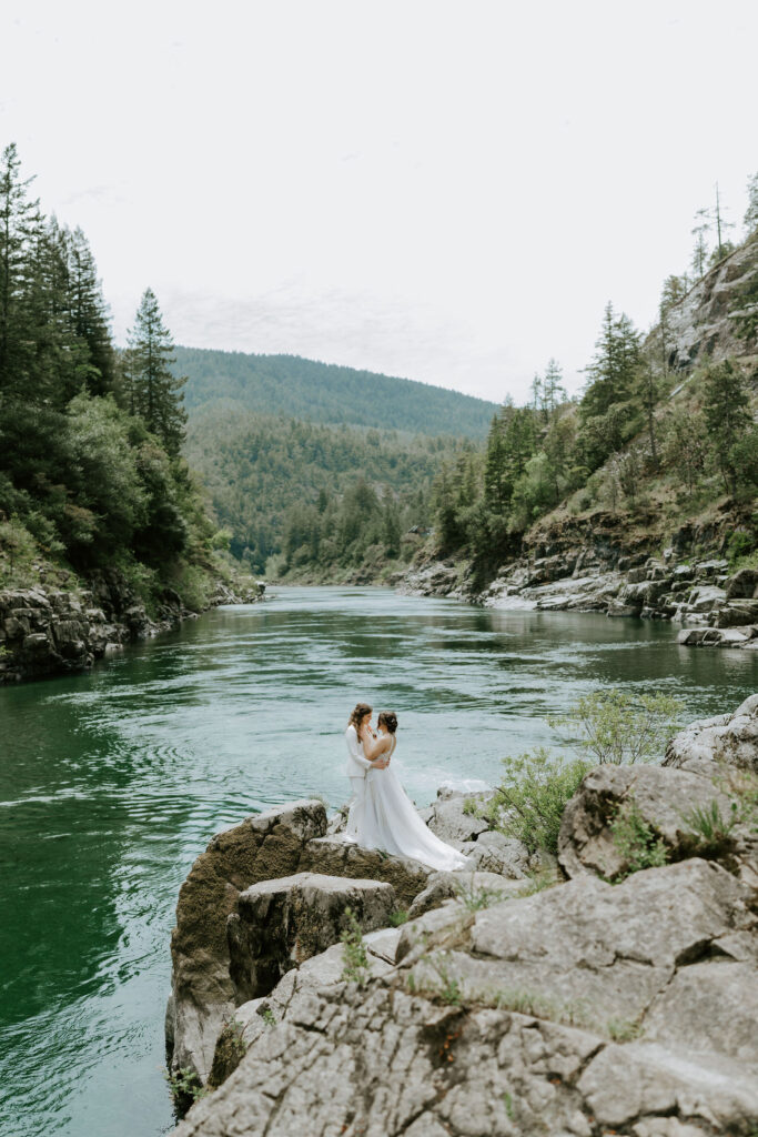 brides posing on a rocky cliff overlooking turquoise smith river