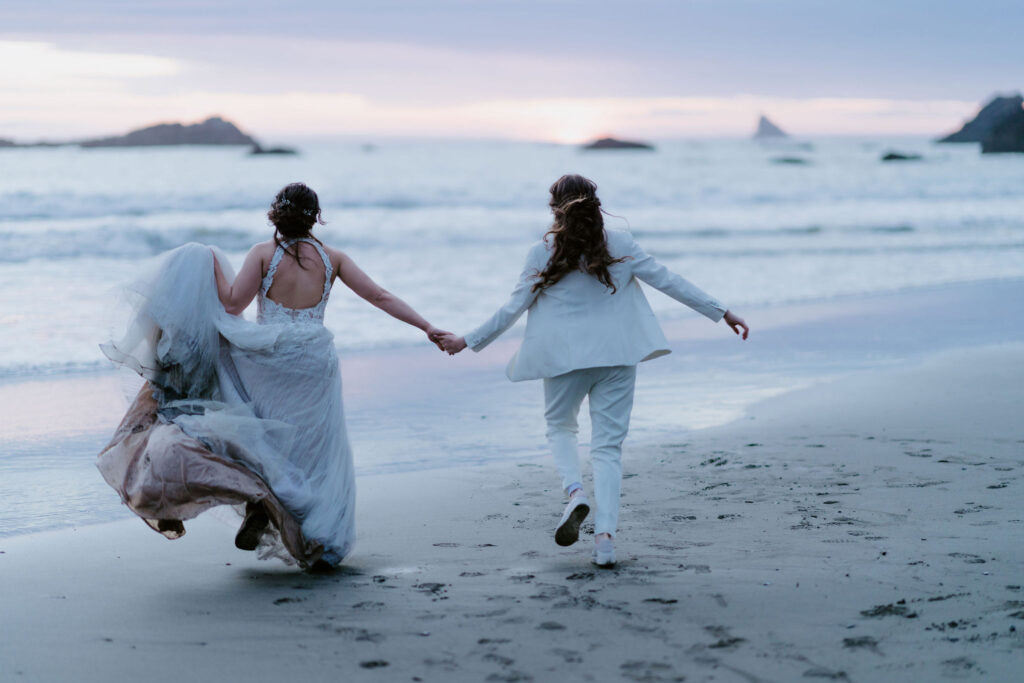 brides running hand in hand around oregon coast at secret beach