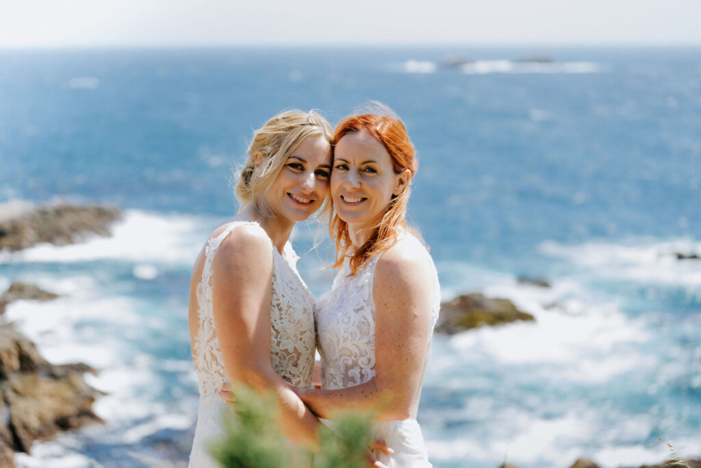 happy brides hugging on a cliff in big sur