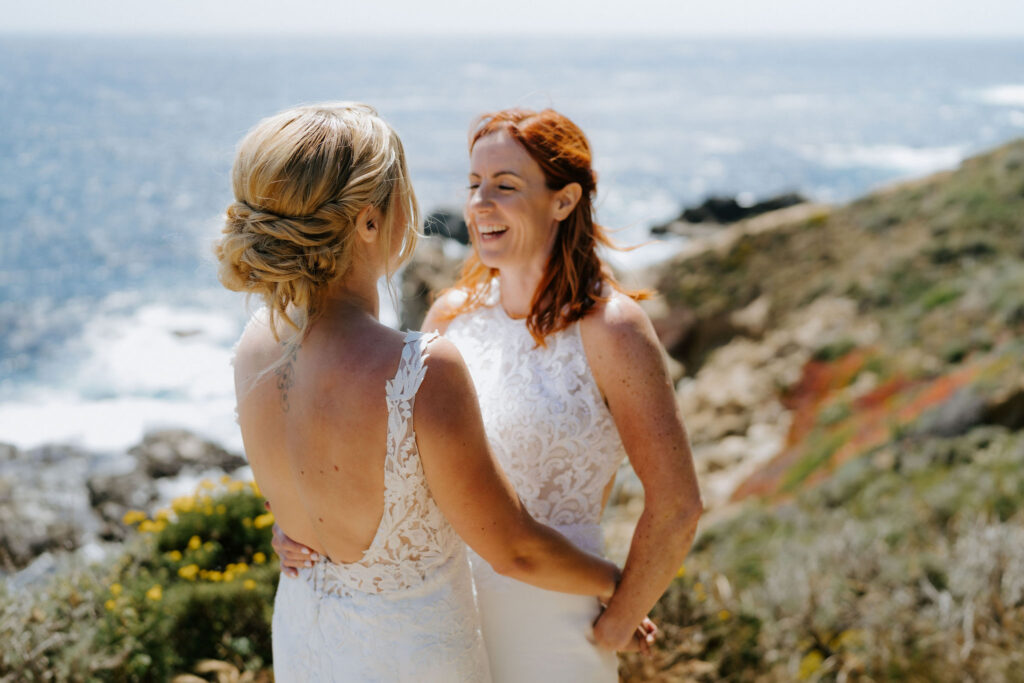 happy brides hugging on a cliff in big sur