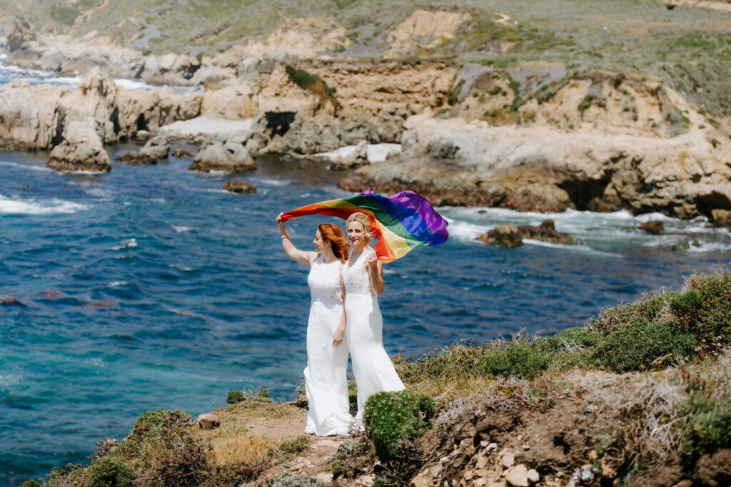 two brides wrapped in a rainbow flag during their luxury elopement in big sur