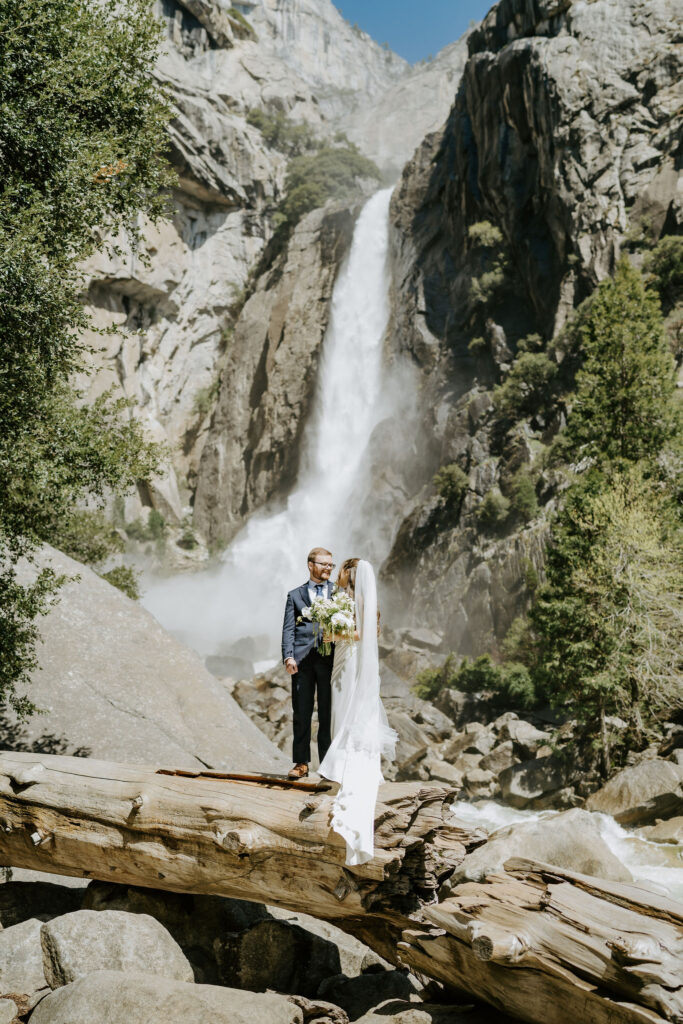 yosemite elopement couple standing on a dry wood log next to a waterfall