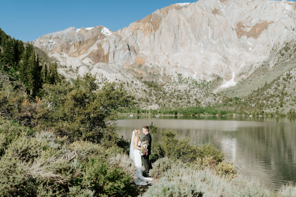 bride and groom next to a lake with rocky mountain views in the background during mammoth lakes elopement