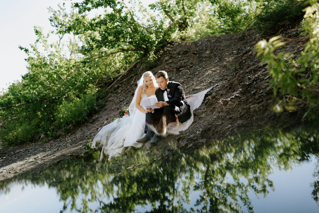 bride and groom reading private letters while picnicking next to a lake 
