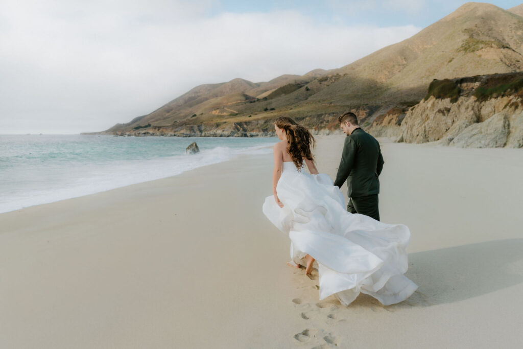 bride and groom walking alongside the ocean in big sur