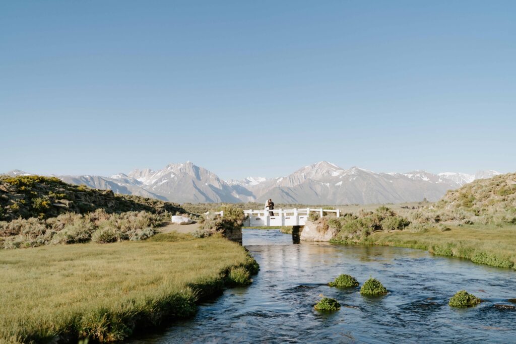 Mammoth Lakes elopement in Northern California crossing a bridge over water at sunrise with the mountains in the background